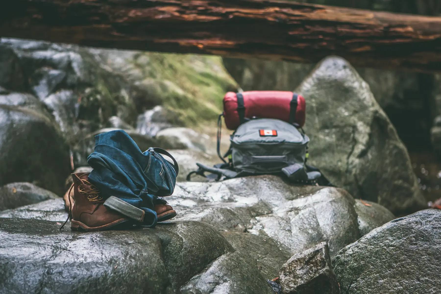 Boots, jeans and a pack resting on wet boulders